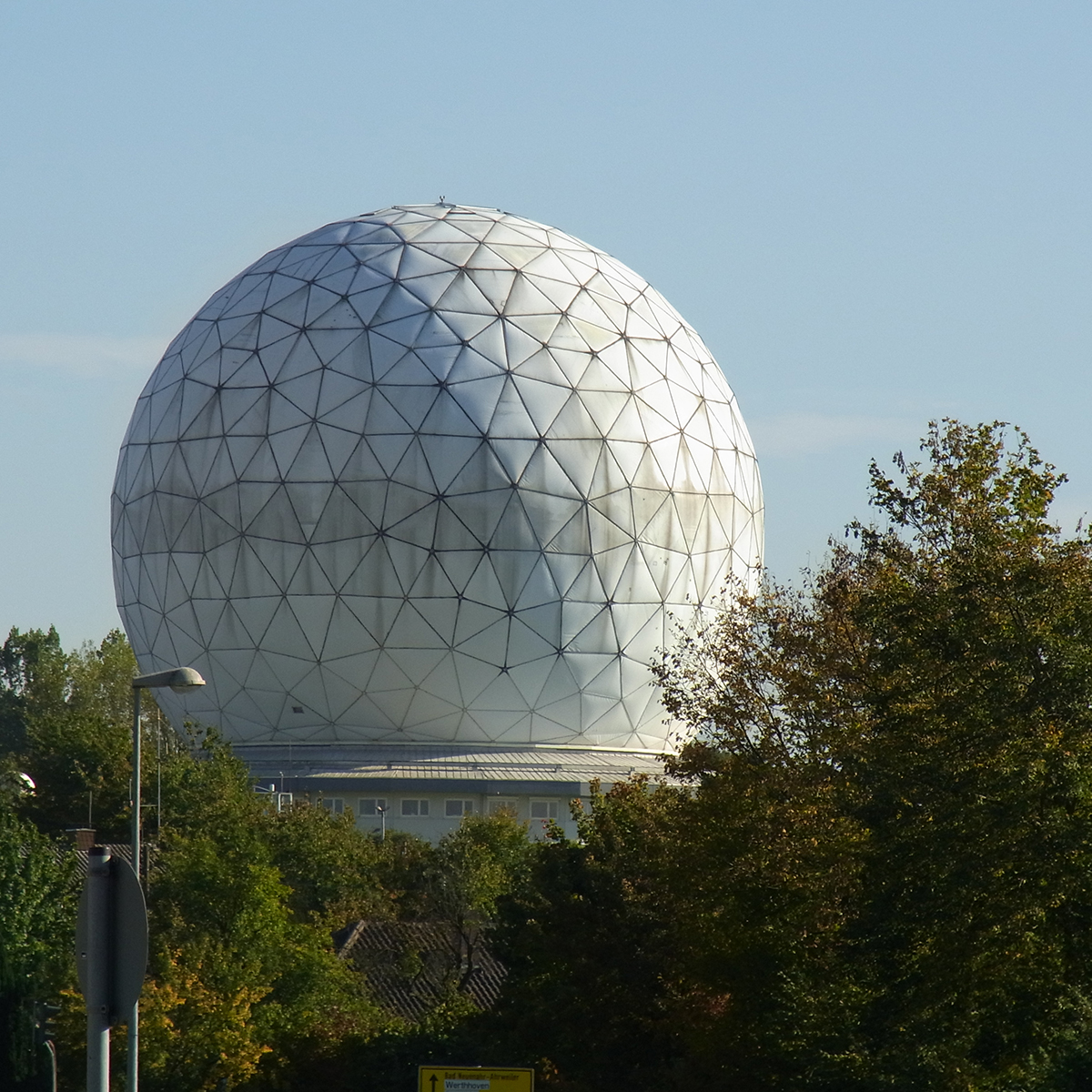 Large white radar dome surrounded by trees under a clear sky