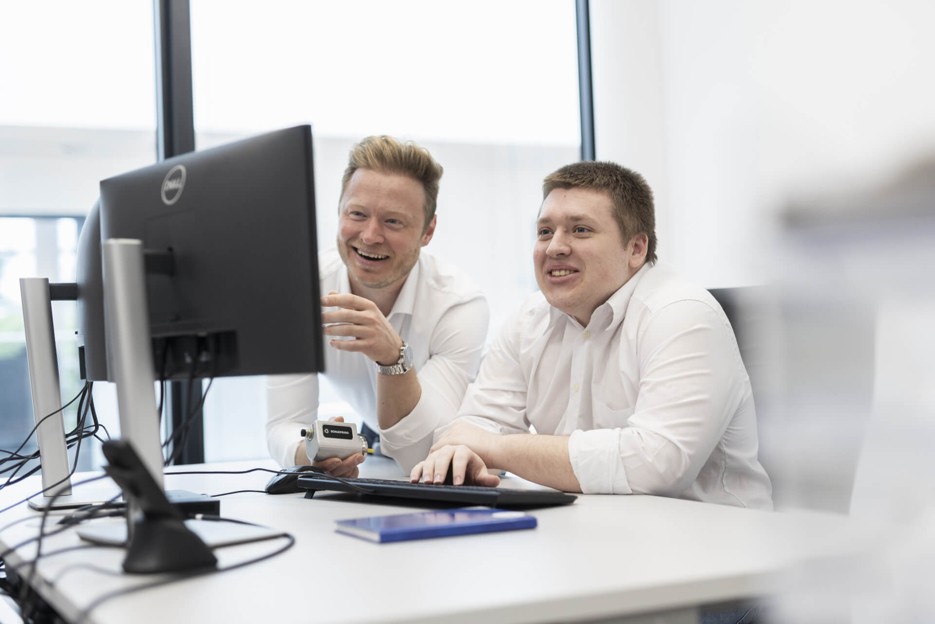 Trainer and trainee working together at the computer in a modern office environment.