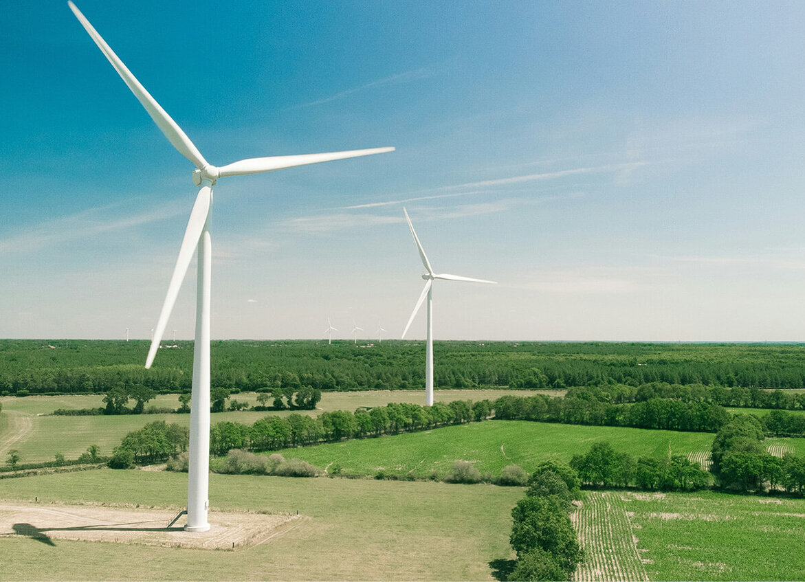 Two large wind turbines stand in green fields under a blue sky.