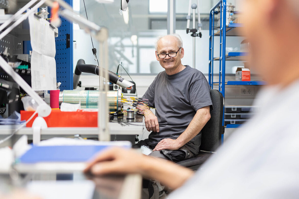 Older SCHLEIFRING employee sits in assembly and smiles.