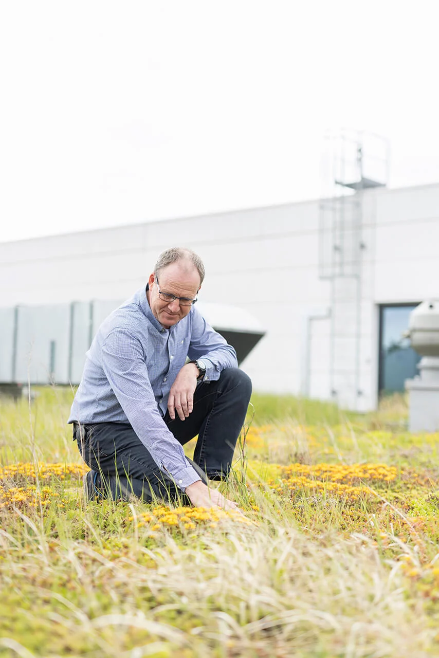 A SCHLEIFRING employee kneels in front of the company building and runs his hand over a green lawn.