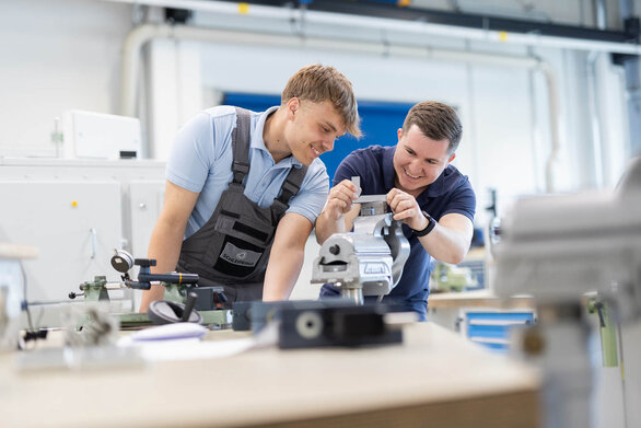 Two young men working together on a metal part in a workshop.