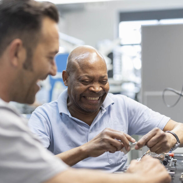 Two employees work together in a good mood on an electronic component in assembly.